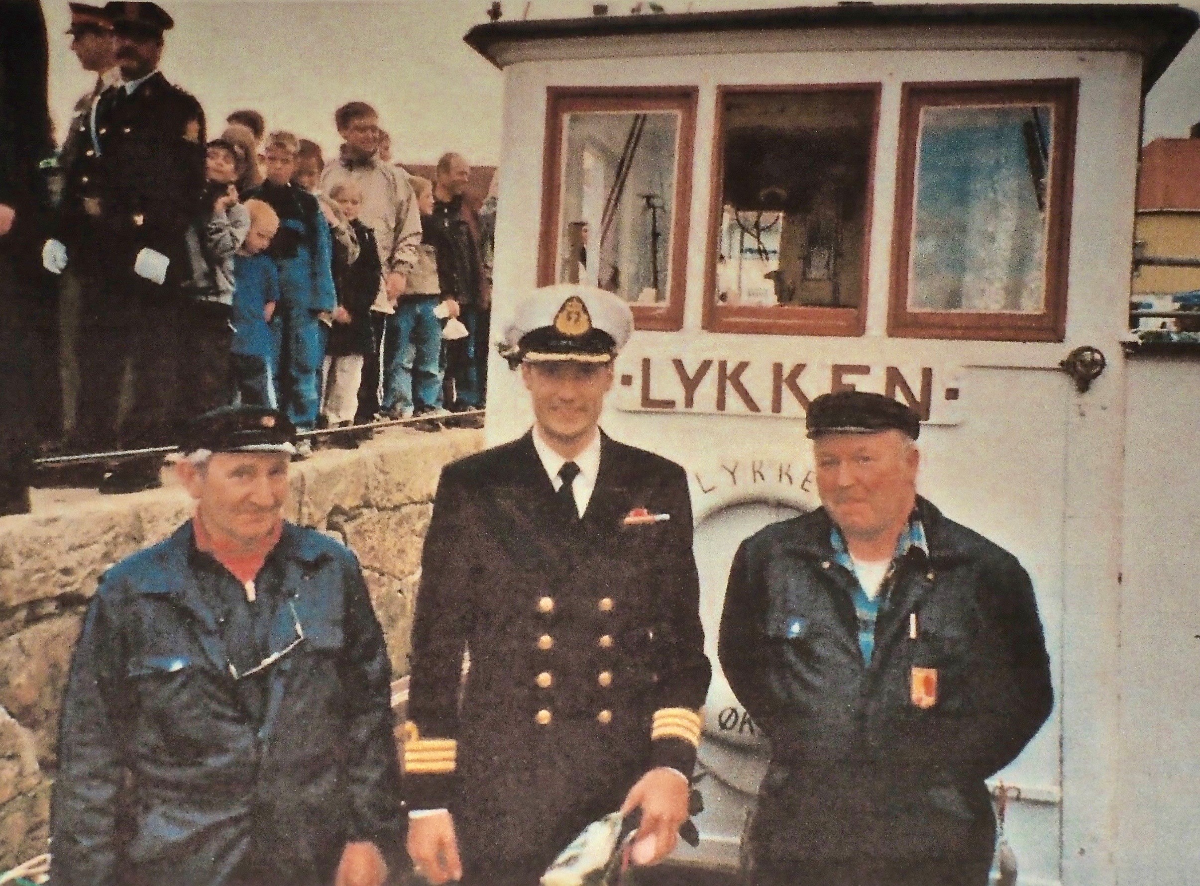Kronprinsen. HKH Kronprins Haakon fattet stor interesse for «Lykken» på sjøheimevernets 50-årsjubileum i Kabelvåg i 1998, og fikk en trivelig prat med Fridtjof Lynghaug (t.v) og Jan Einar Andersen. Sikkerhetsvaktene i bakgrunnen har etter hvert skjønt at guttene fra Øksnes er helt ufarlige, og kan slappe av. (Fotograf ukjent).